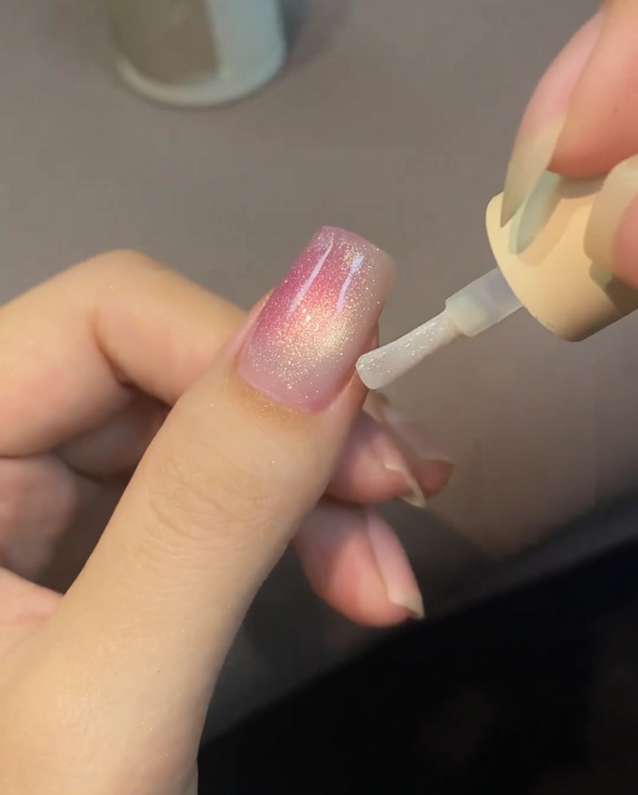 A close-up view of a nail surface with small, pearl-toned water droplets blooming on a wet top coat base.
