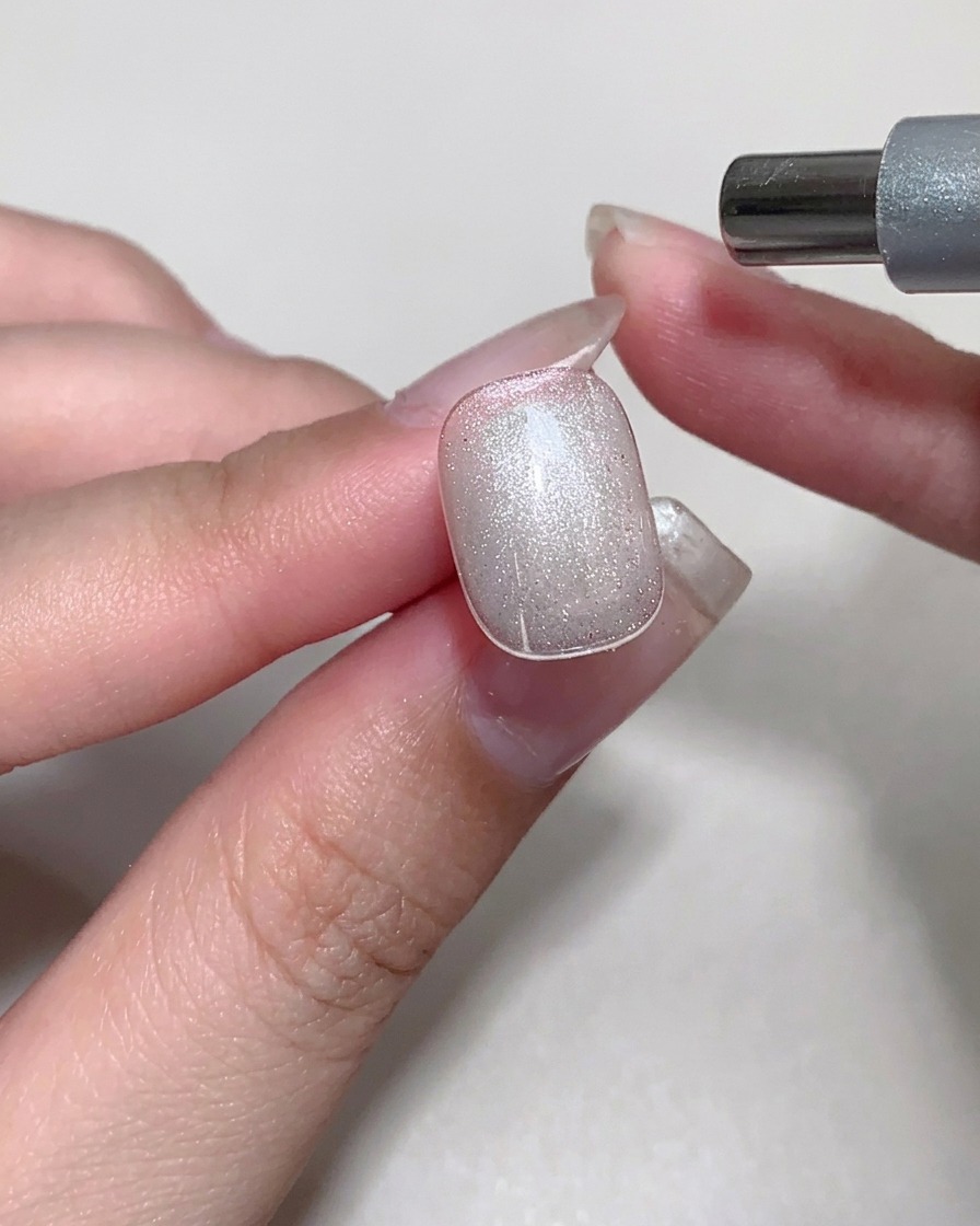 A magnet being used over a nail with wet cat eye gel to create a glass-like shimmer effect.