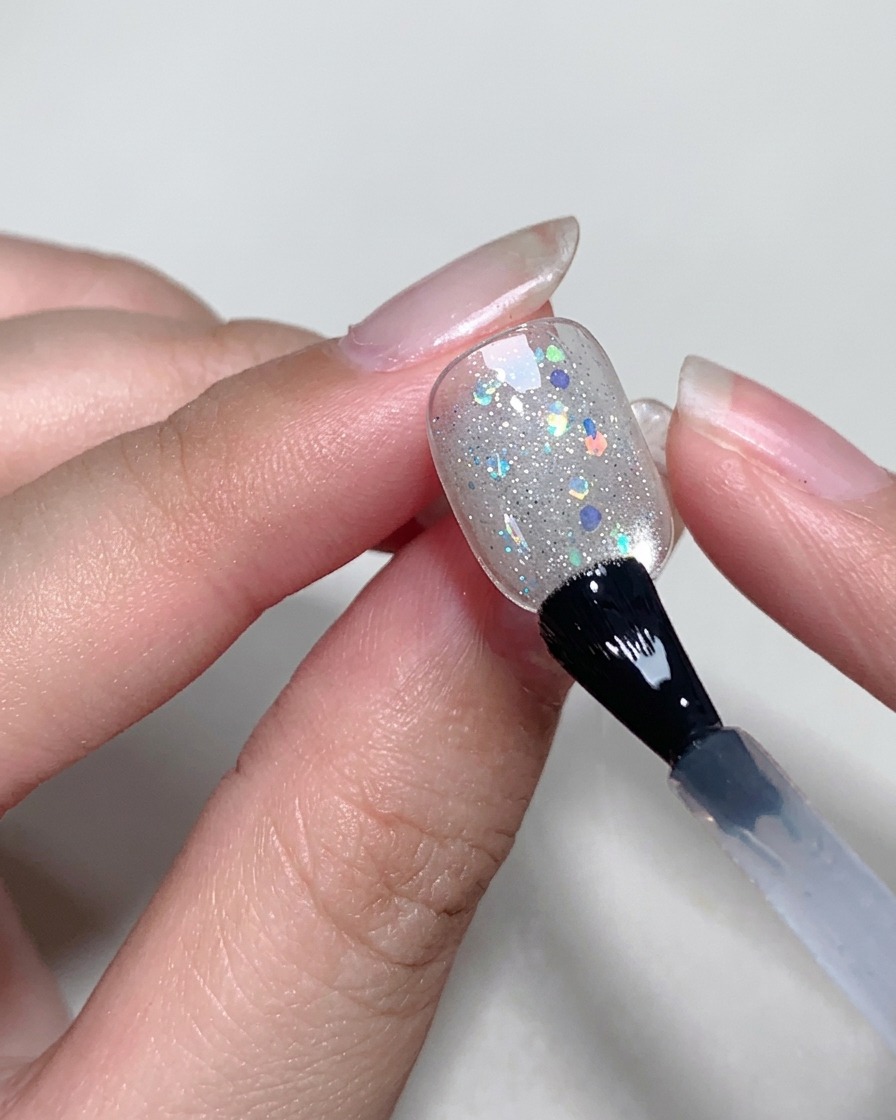 Applying a clear, thin layer of blooming gel onto the surface of the nail using a brush.