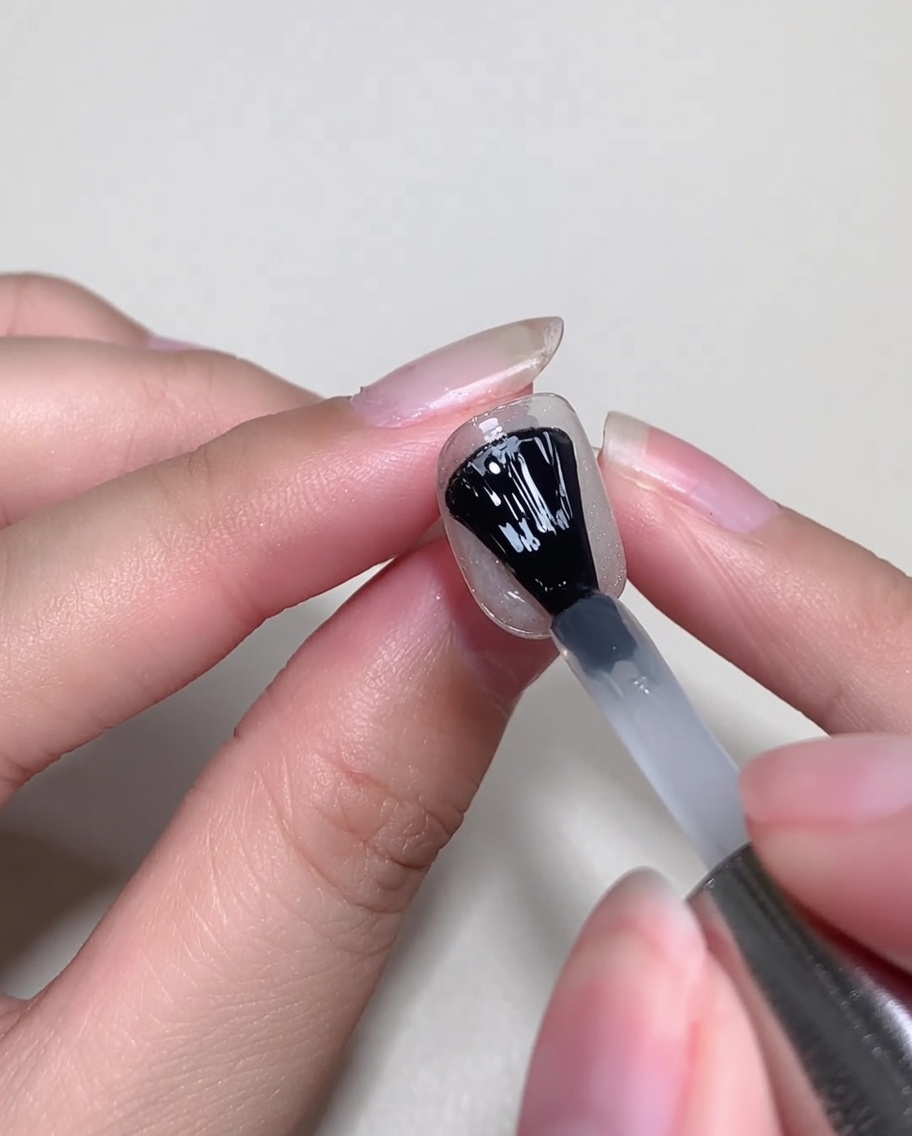 A gel polish brush applying a thin layer of clear blooming gel over a decorated nail.