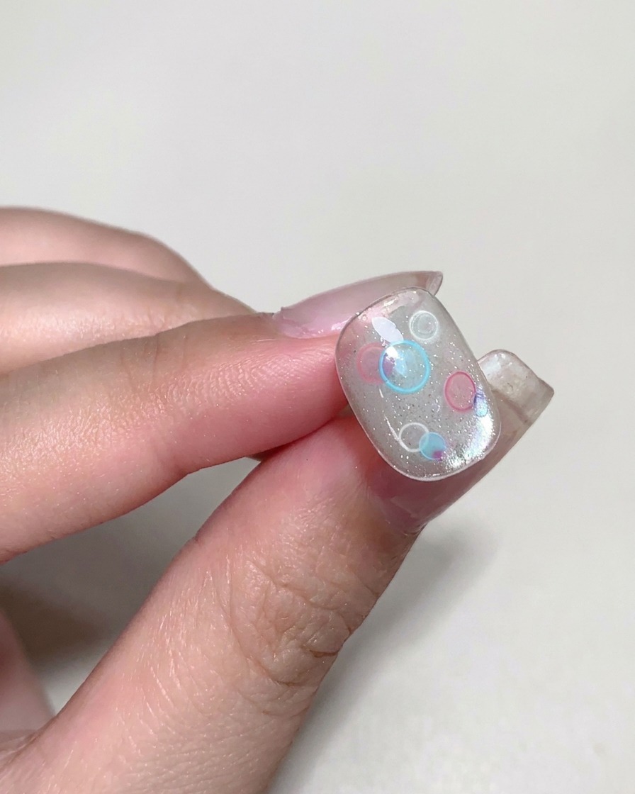 A brush applying a clear, viscous builder gel over a decorated nail.