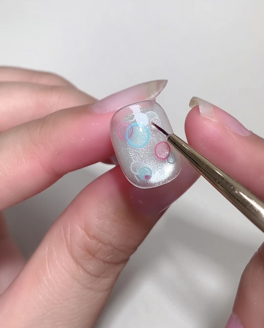 A fine-tipped brush carefully placing small, clear, circular sequins onto a nail.