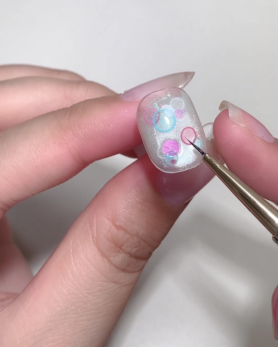 A thin liner brush drawing a small, white cross-shaped star on a manicured nail.
