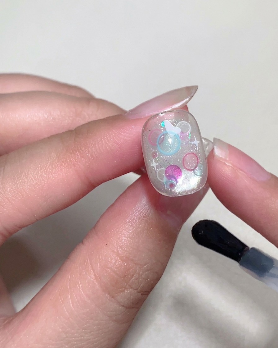 A brush applying a final glossy top coat to the nail surface.