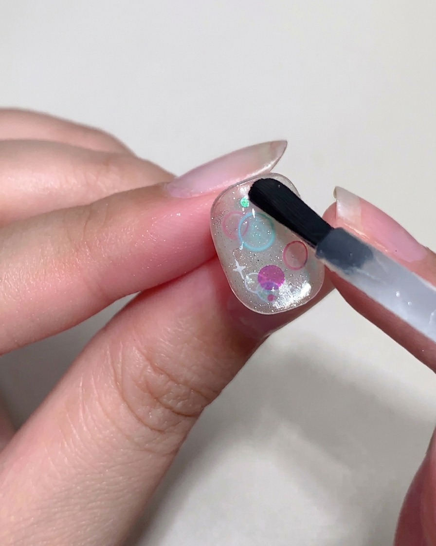 A detailing brush using thick top coat to form small, raised bubbles over sequins on the nail.