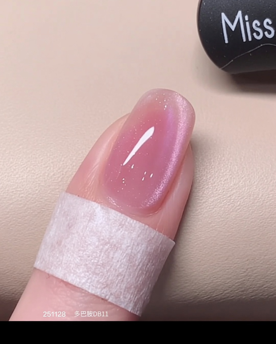 A brush applying a fresh, wet second coat of pink cat eye polish over the previously cured layer.