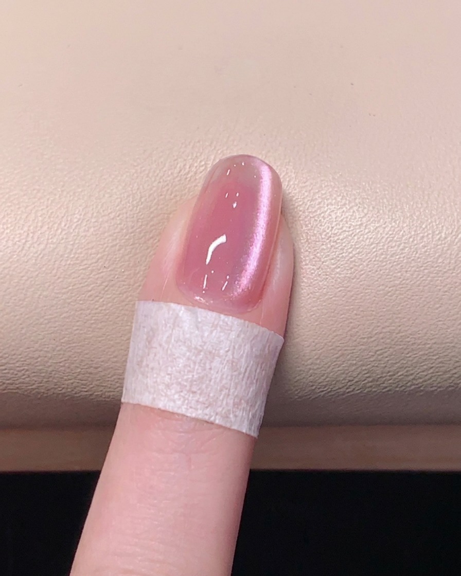 A brush applying a clear, glossy top coat over a pink magnetic cat eye gel nail.