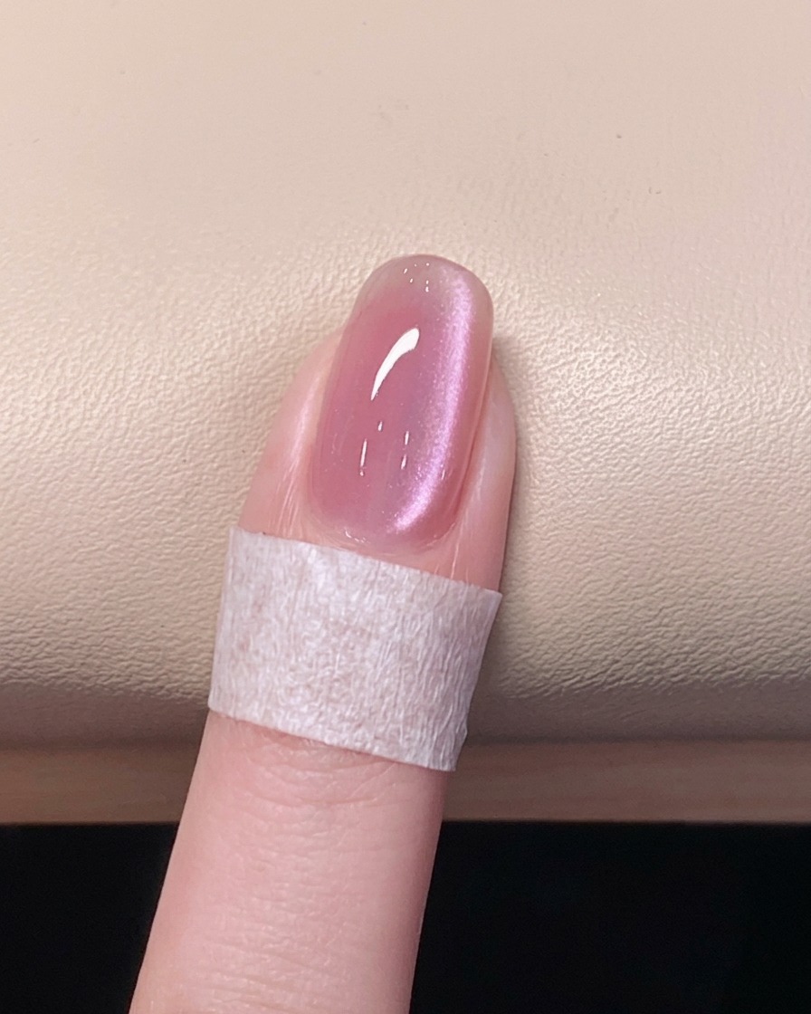 A hand resting inside a UV/LED nail lamp with the light turned on, curing the final top coat.