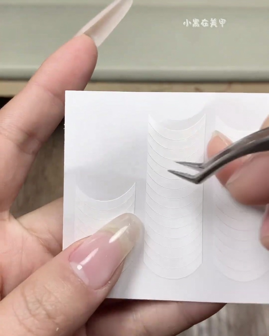 A hand applying a white French tip sticker guide onto a clean natural fingernail.