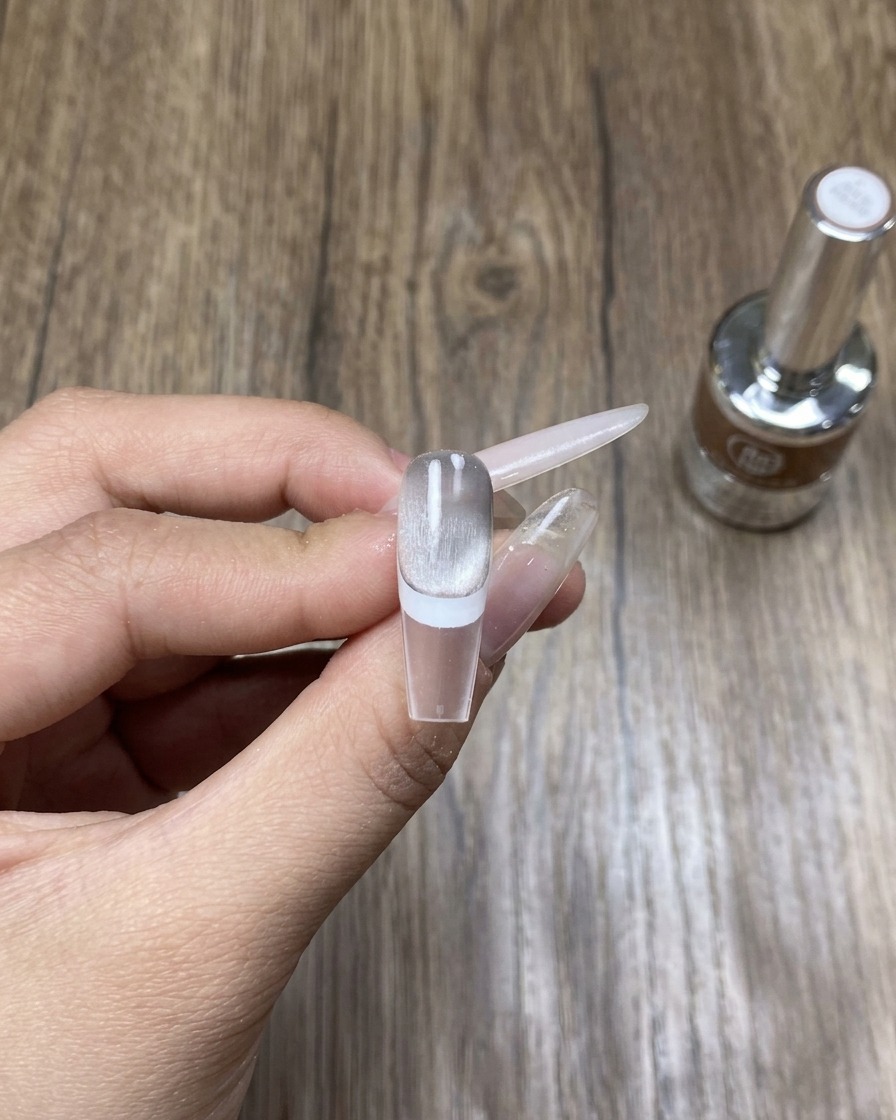A hand resting inside a professional UV/LED lamp, curing the freshly applied cat eye nail art.