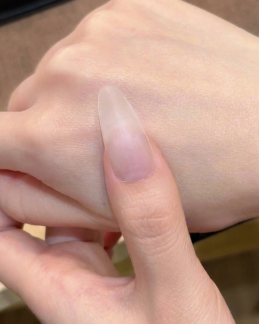 The first layer of sheer nude pink gel being applied to the nail with a polish brush.