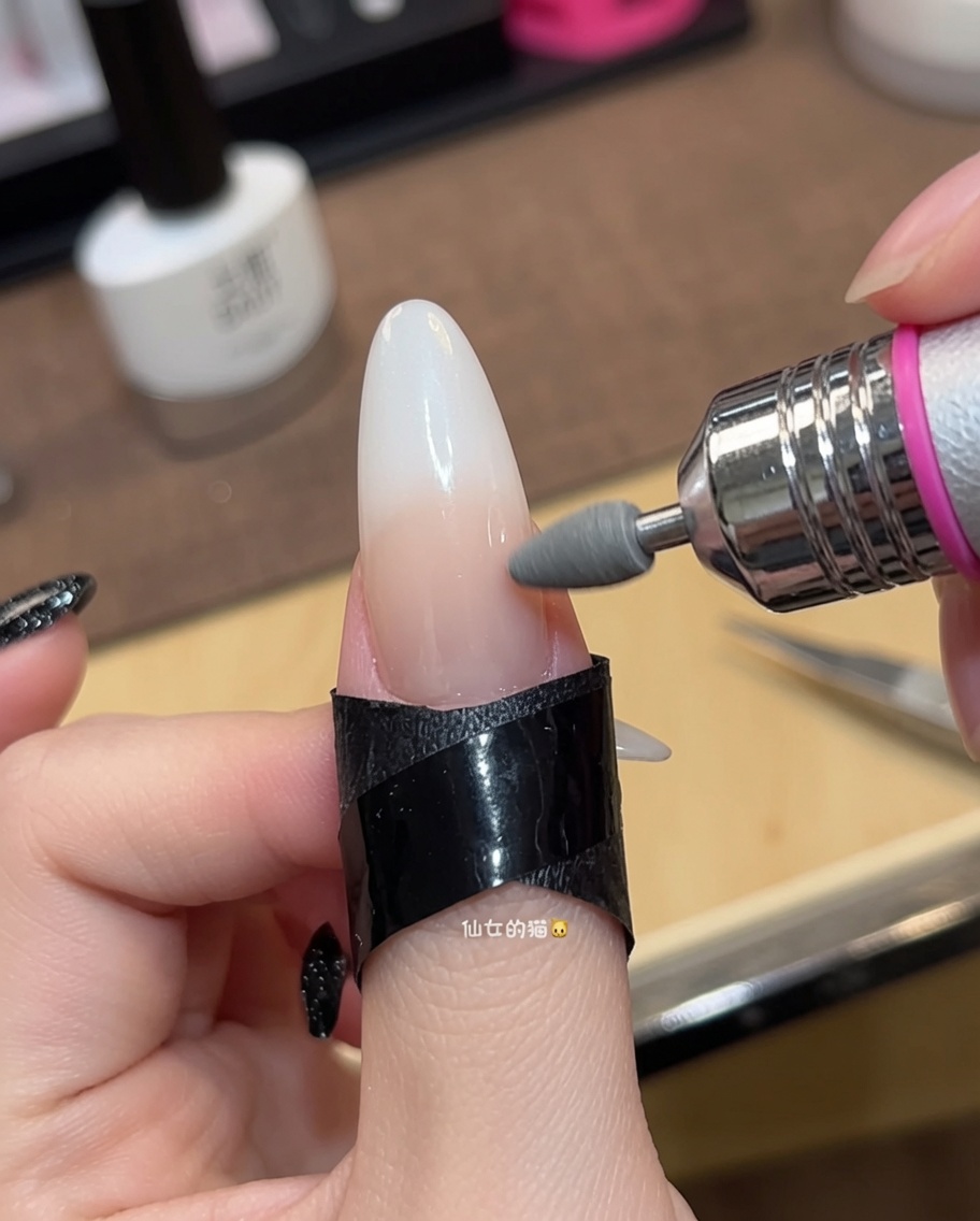 Close-up of a brush applying a second coat of sheer nude gel polish to a fingernail.