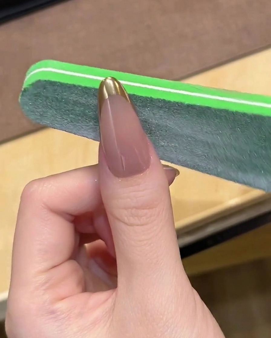 A nail file gently smoothing the tip of a chrome French manicure.