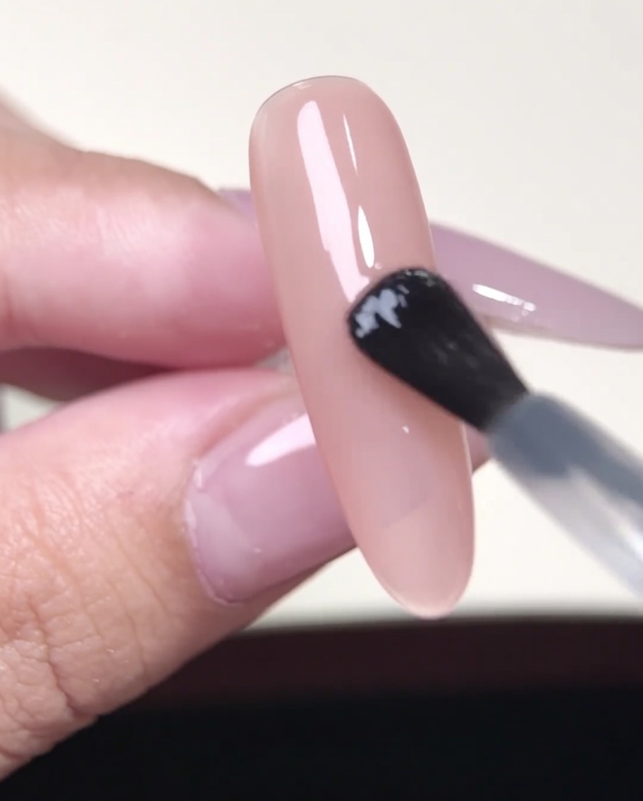 A pair of tweezers holding a French tip sticker over a nude-colored gel nail.