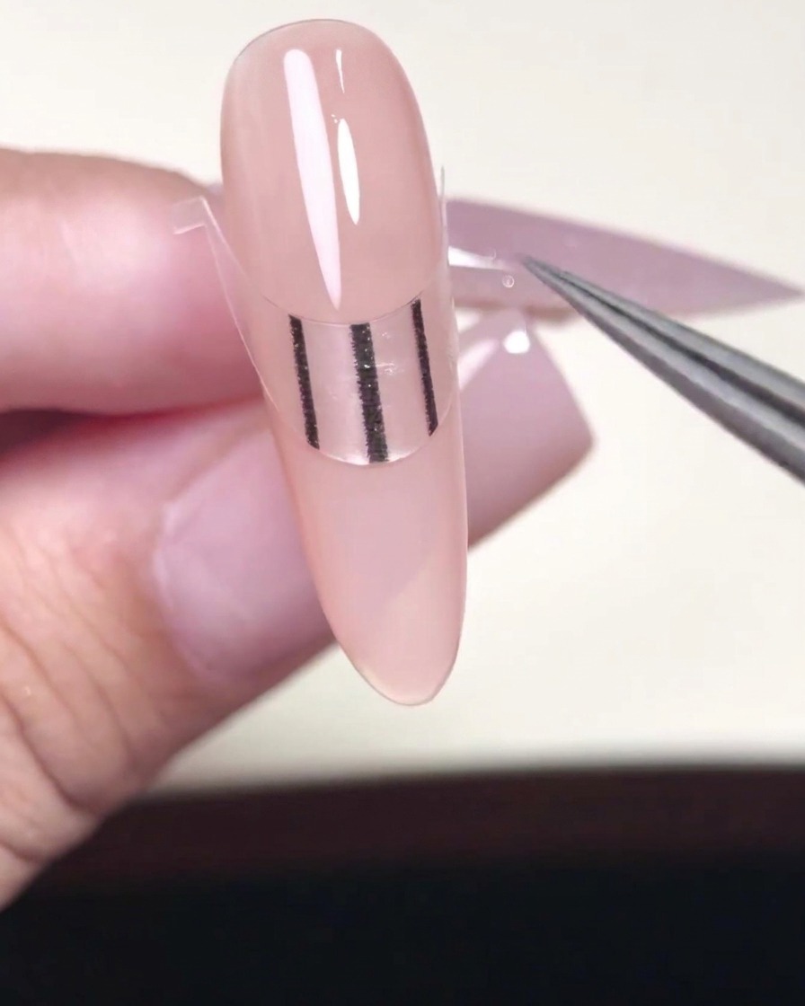 A metal tool pressing the edges of a French tip sticker firmly onto a gel-painted nail.