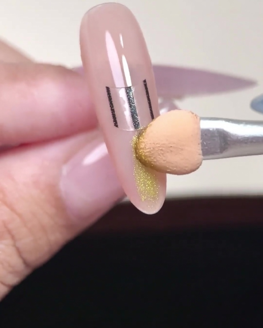 An eyeshadow applicator applying gold chrome powder to the tip of a nail below the French sticker.