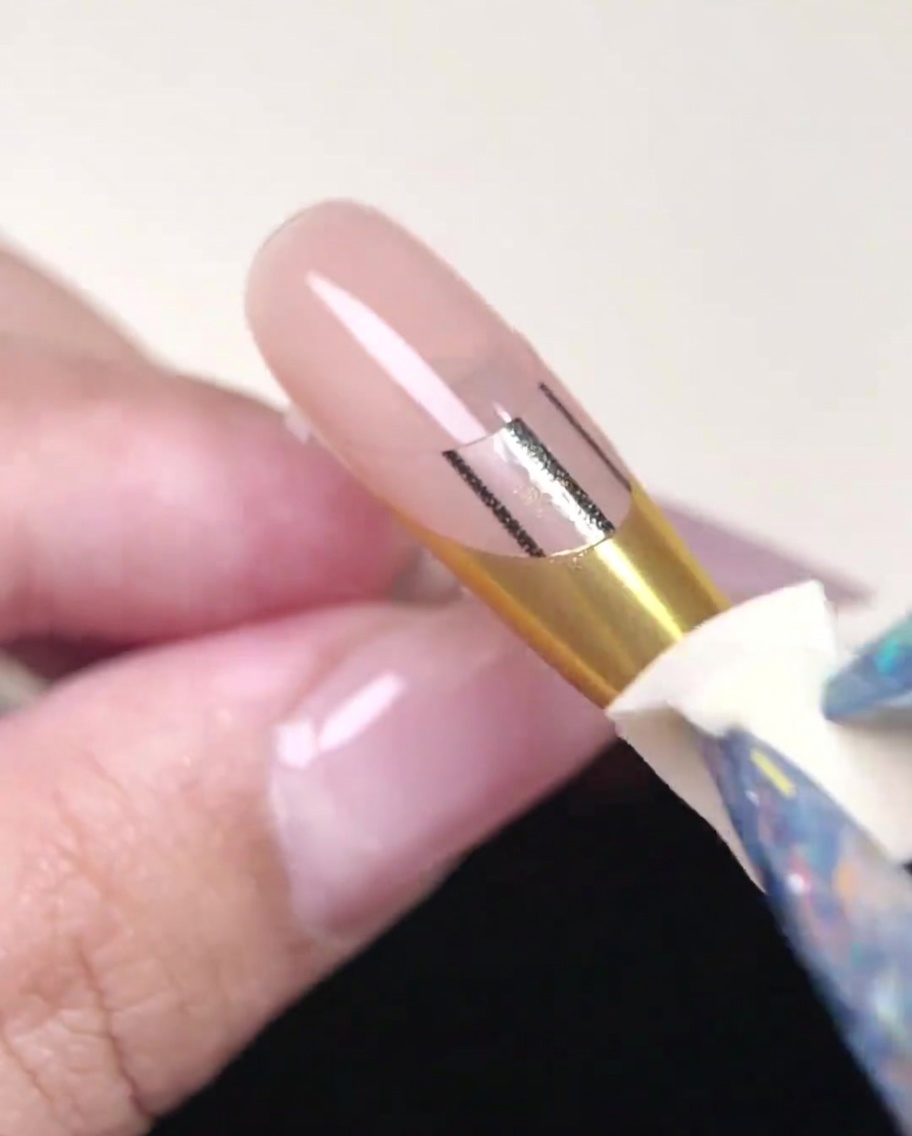 A clean sponge being used to burnish gold powder on a nail tip.