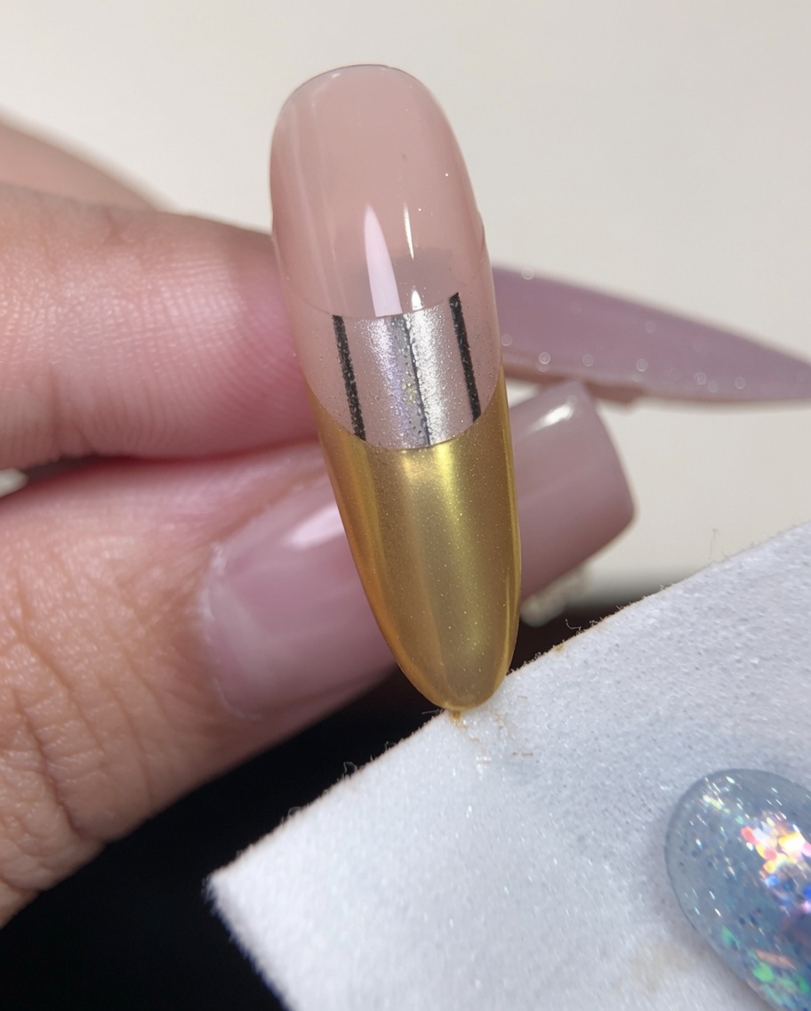 A close-up of a lint-free wipe being used to clean the sides and tip of a nail with a gold chrome French tip design.