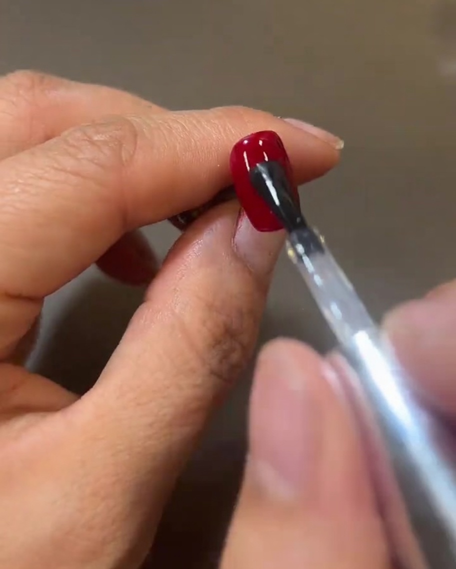 A nail brush applying a fresh, shiny layer of clear top coat over the red gel, creating a wet, reflective surface.