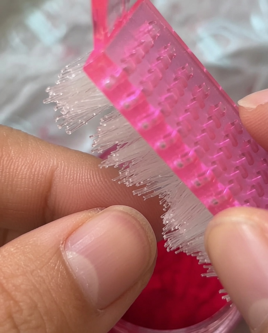 A close-up shot of a pink manicure brush sweeping over a red fuzzy-coated nail.