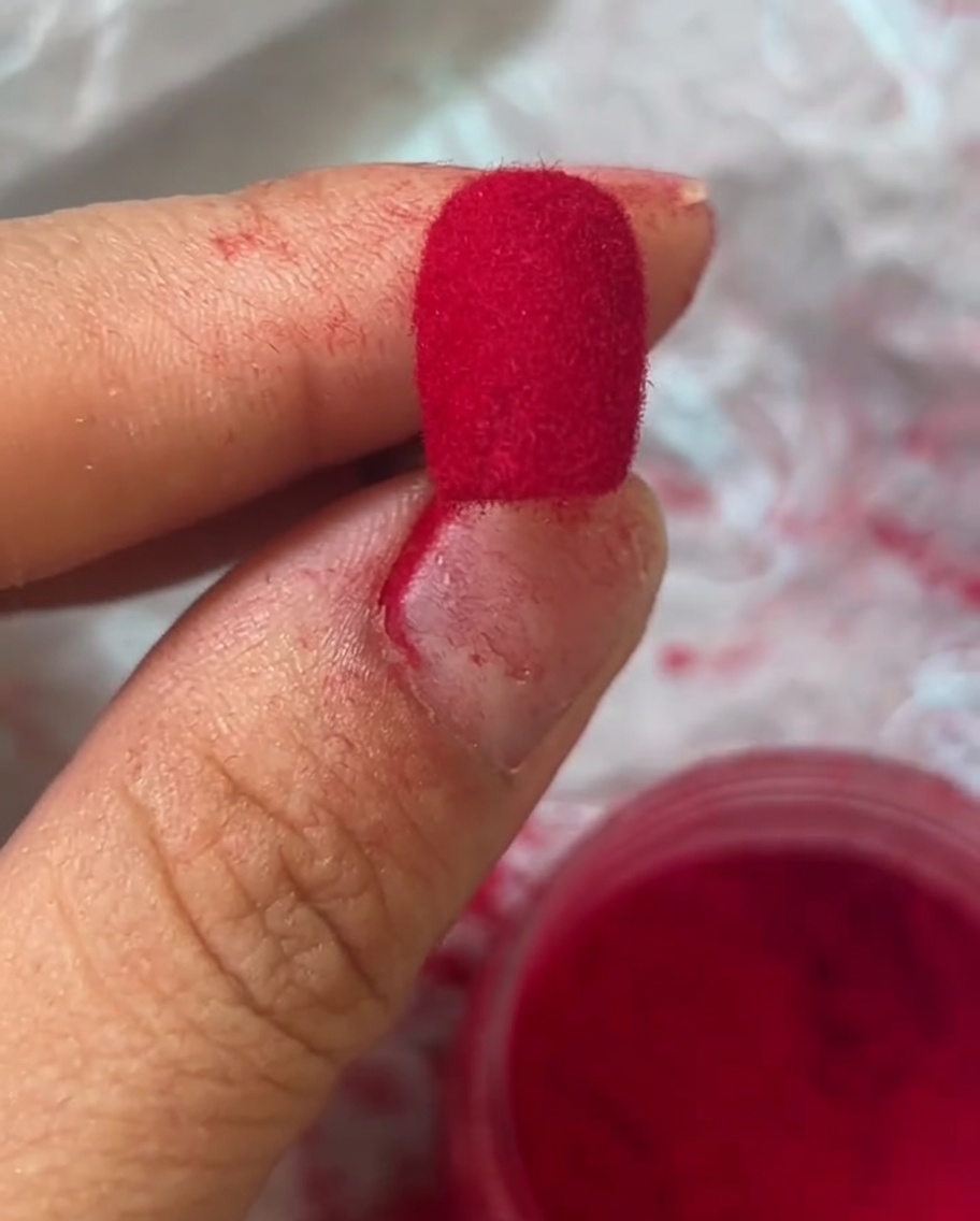 Macro view of a fingernail covered in a vibrant red, velvet-textured finish.