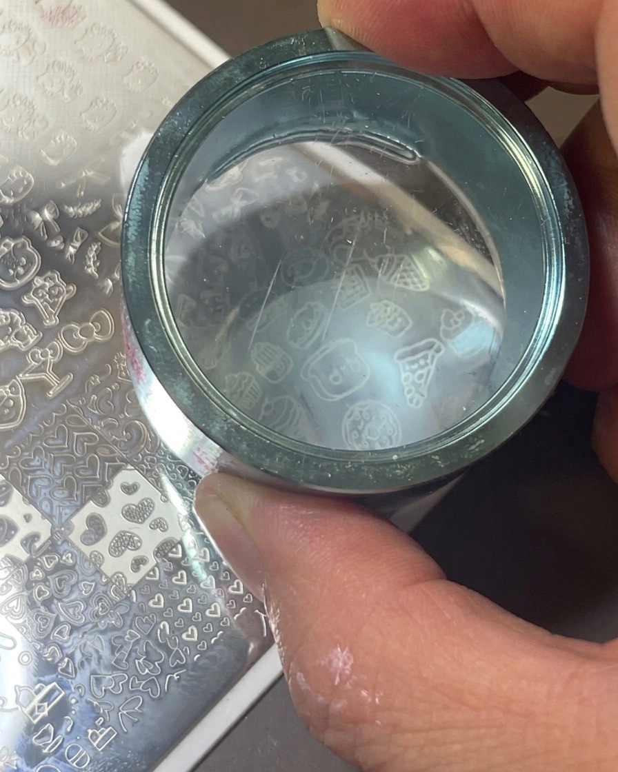 A clear cylindrical stamper being pressed onto a metal plate to transfer a white icon design.