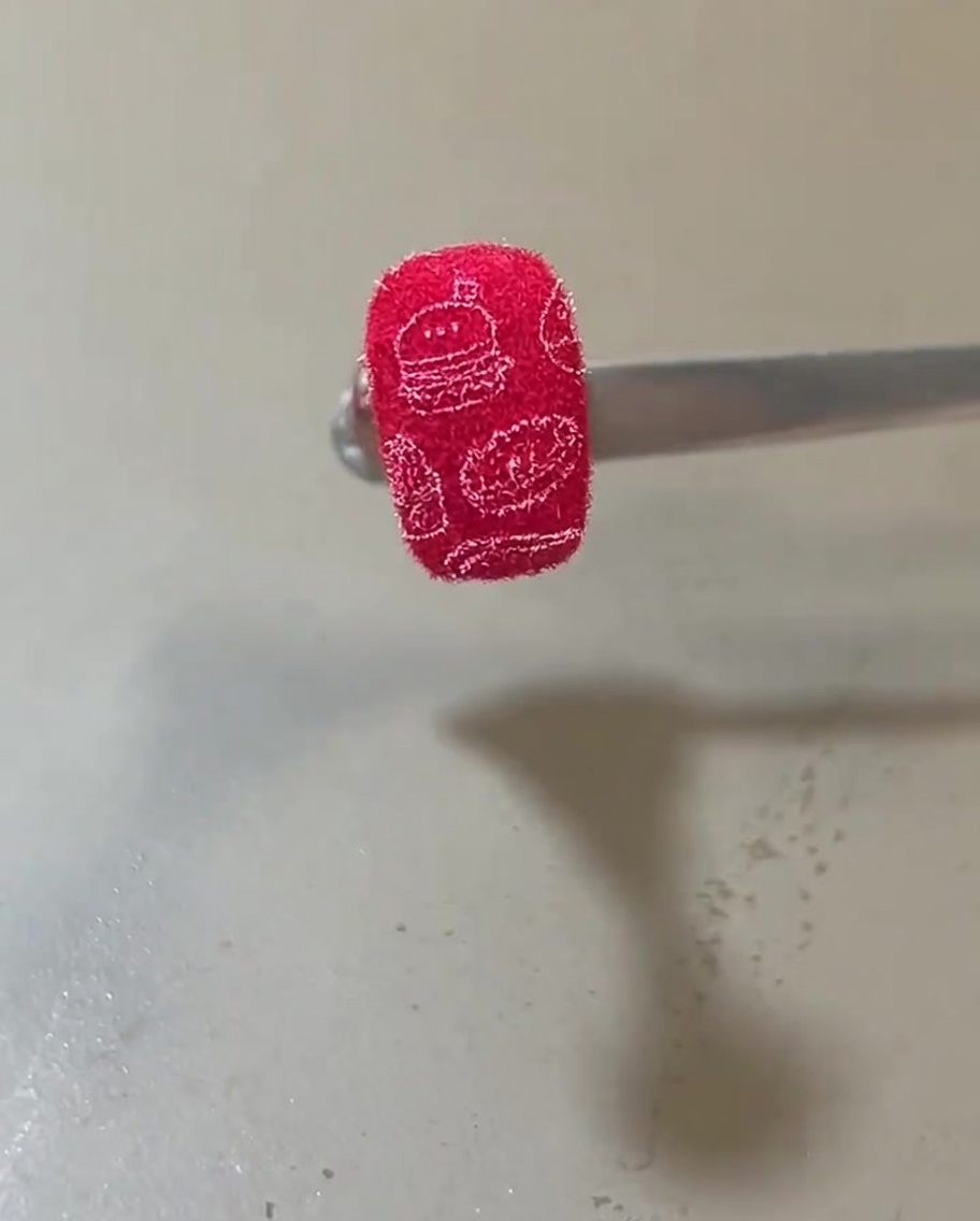 A finished nail with a vibrant red fuzzy texture adorned with white stamped illustrations of burgers and food items.