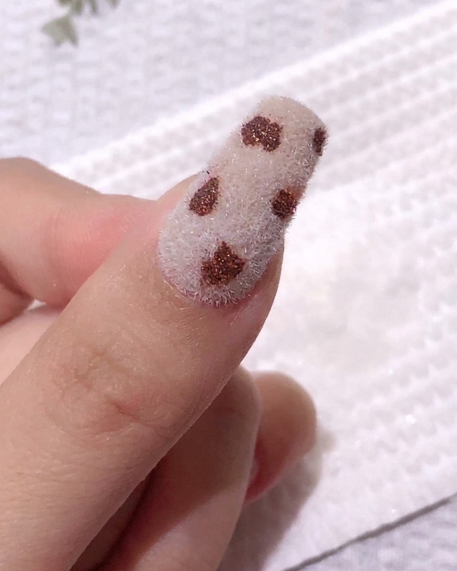 A nail featuring several dark coffee-colored spots on a white velvet surface, showing the result after lightly wiping to set the design.