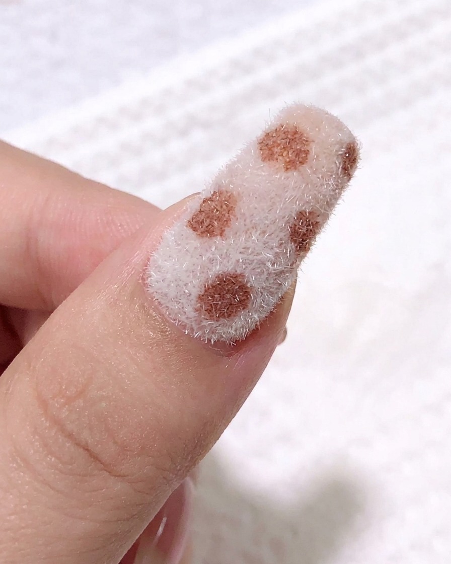 A close-up view showing a fine liner brush applying black gel to create leopard spot patterns over the textured nail surface.