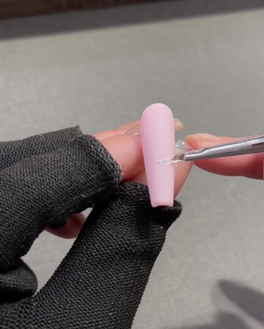 A fine detail brush applying textured white plaster gel to create a French smile line on a pink nail base.