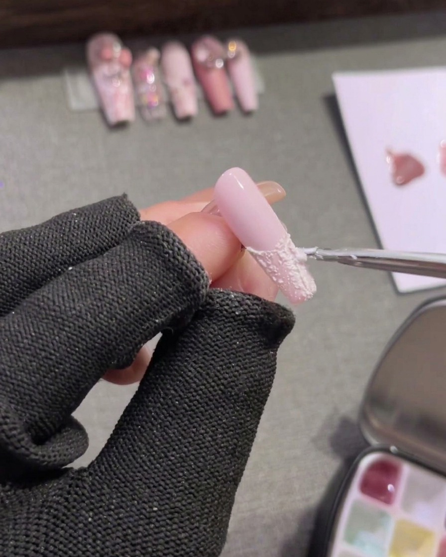 A detail brush filling in the tip of a pink nail with opaque white plaster gel.