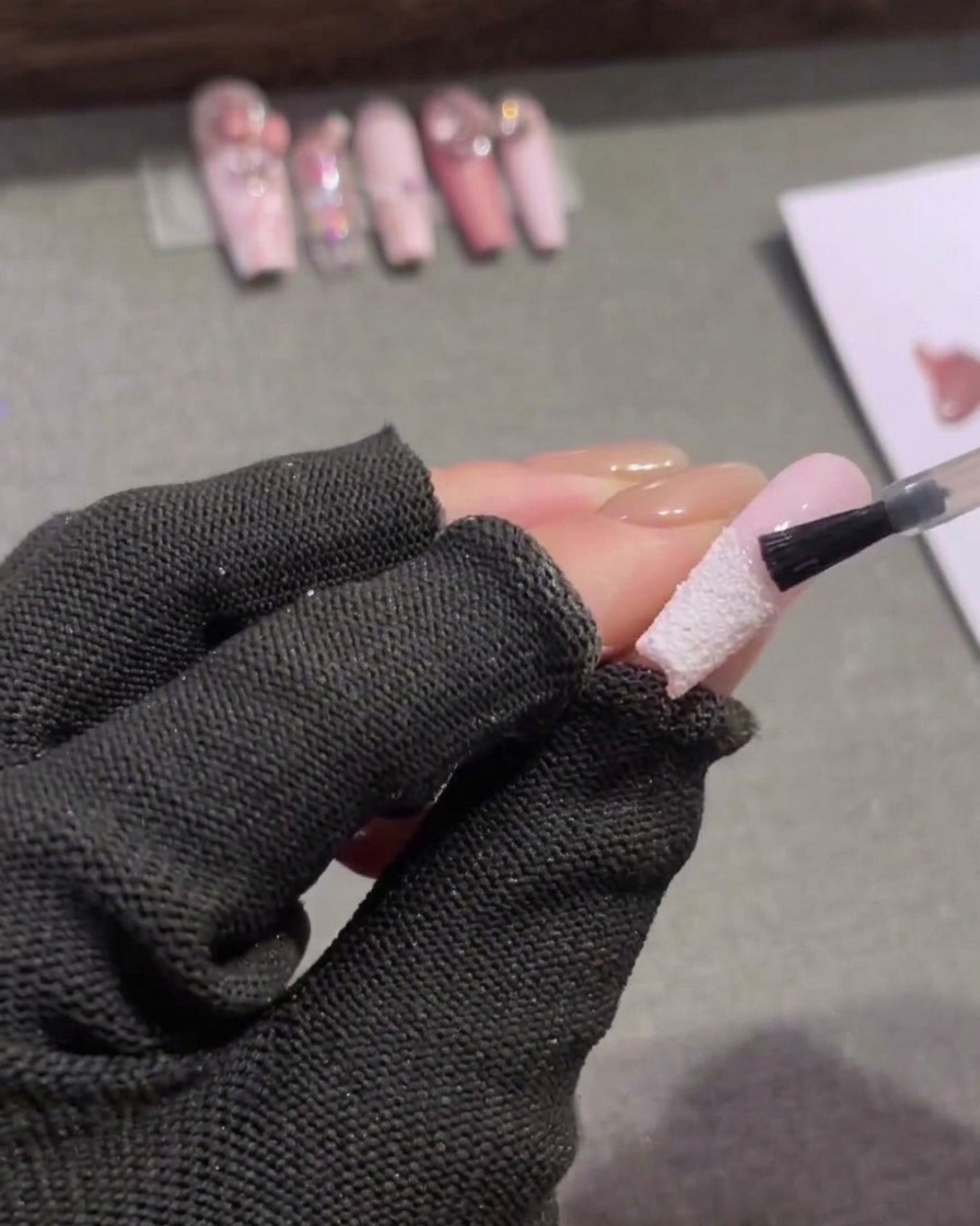 A small nail brush applying a clear matte top coat to the pink upper half of an almond-shaped nail, stopping just above a textured white French tip.