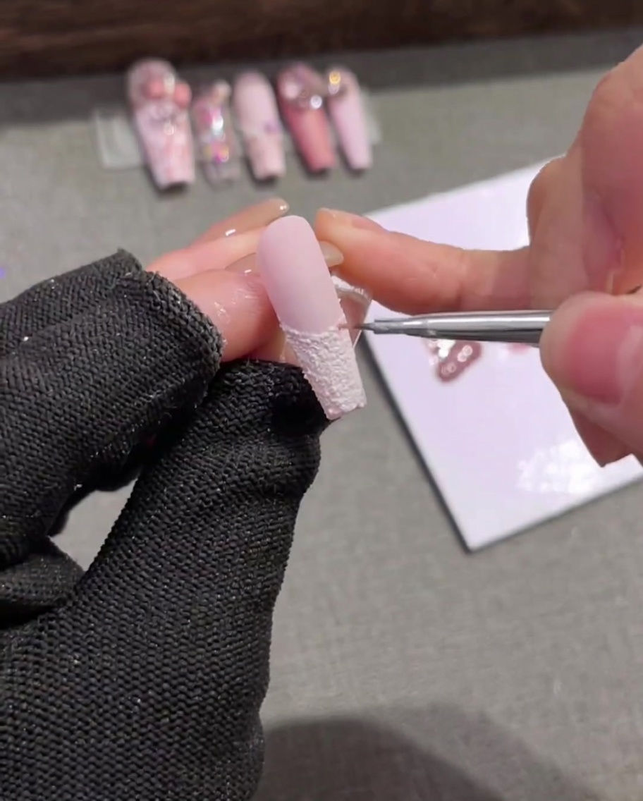 A close-up of a liner brush applying delicate light pink vertical stripes over a white textured French-tipped nail.