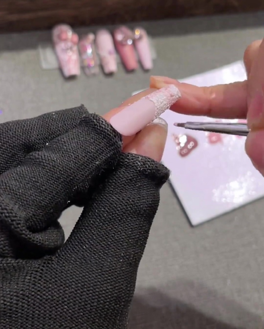 A fine nail brush drawing horizontal light pink lines across a textured white tip, intersecting vertical lines to create a grid.