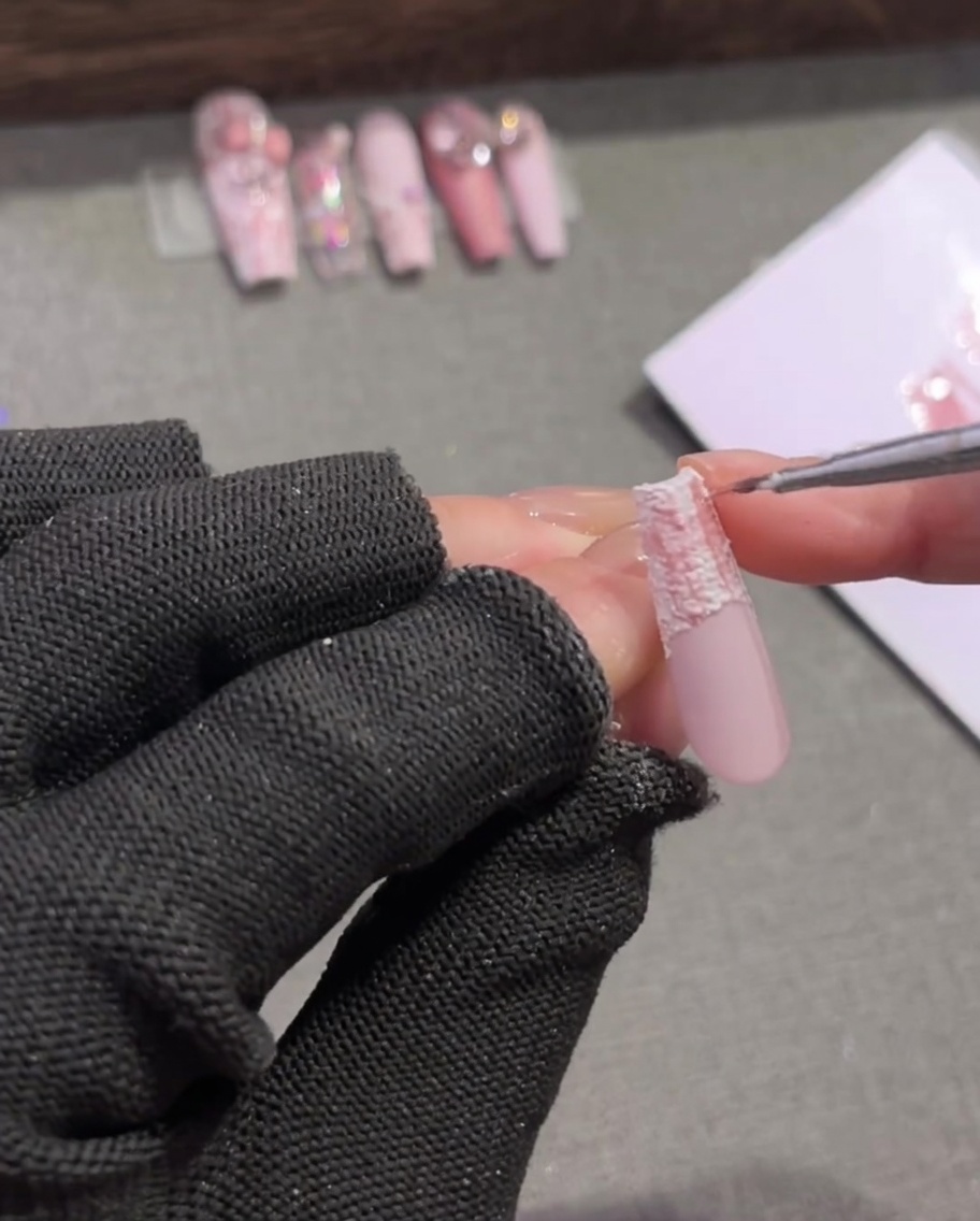 A detail nail brush adding thin, dark brown intersecting lines to a pink and white plaid nail pattern.
