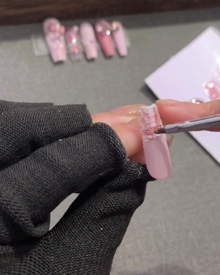 A fine brush applying a mid-tone pink gel to the upper edge of a plaid nail tip to soften the transition.