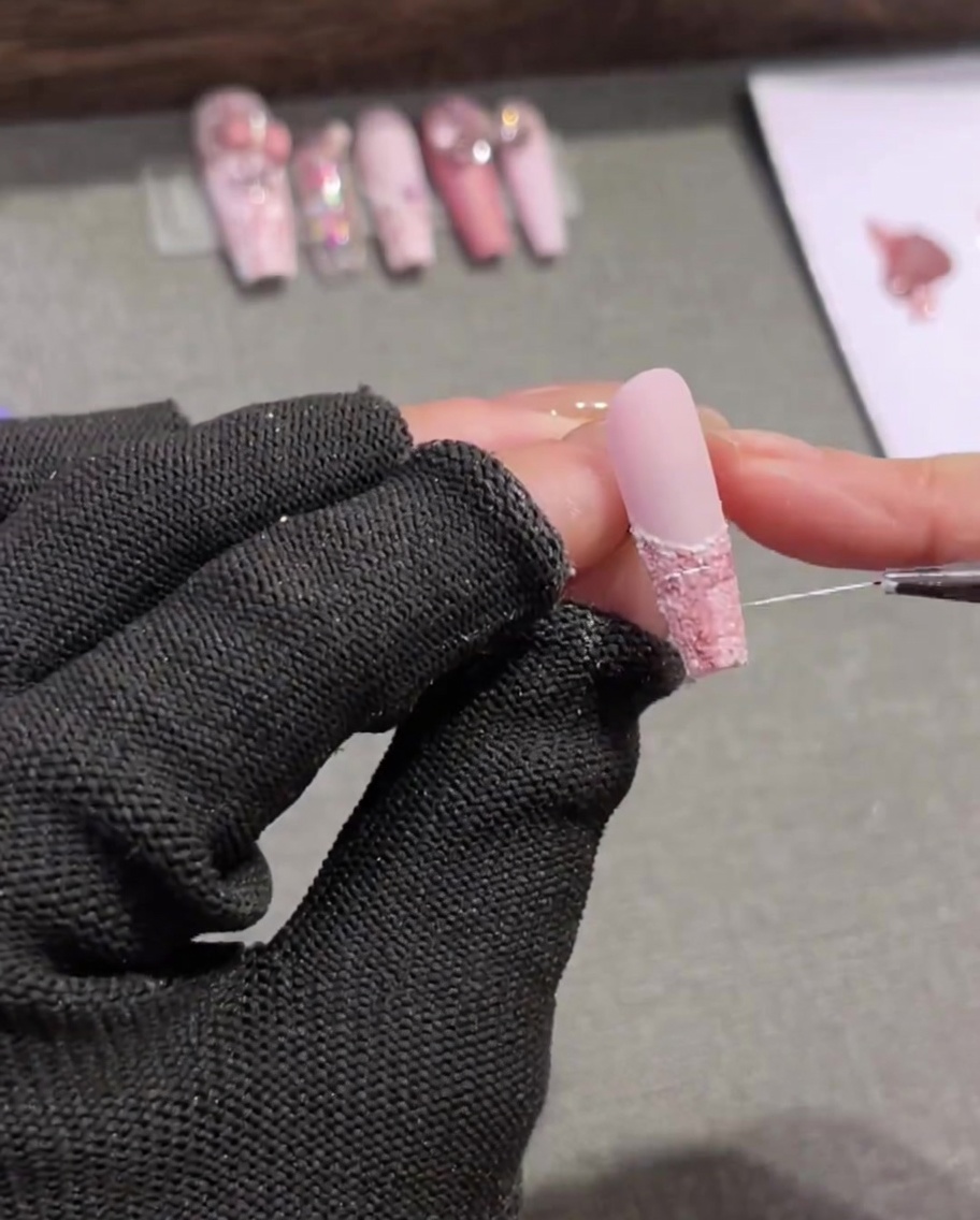 A very thin, long liner brush sweeping delicate, random white lines across a pink and brown tweed nail design.
