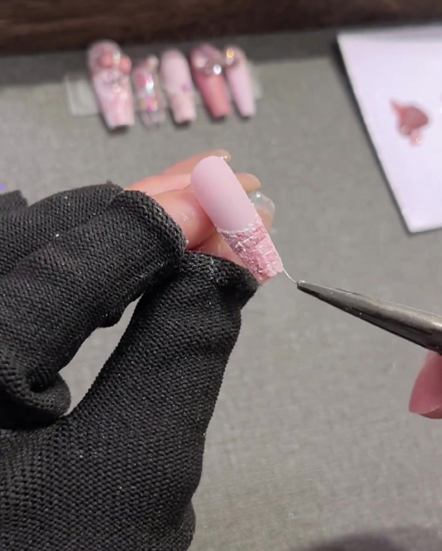 A liner brush carefully drawing thin white horizontal lines across a pink-and-white plaid nail design.