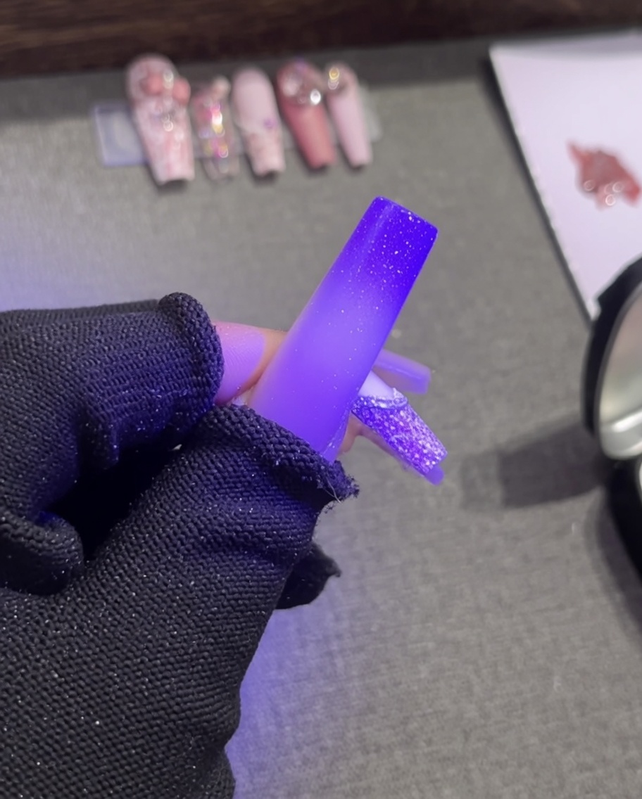 Tweezers placing a small, elegant white pearl bead onto the wet white plaster gel outline of a French tip.
