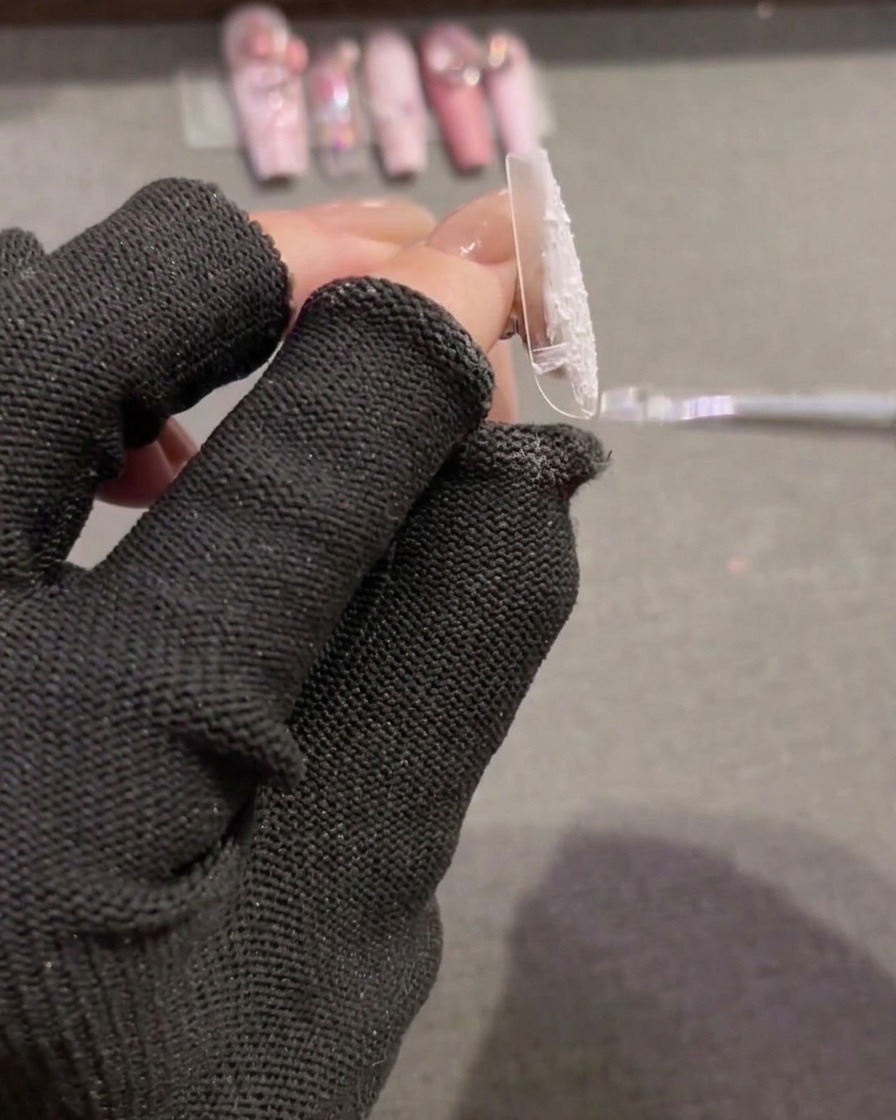 A brush spreading white, textured plaster gel over a new clear nail tip to create a full-coverage base.