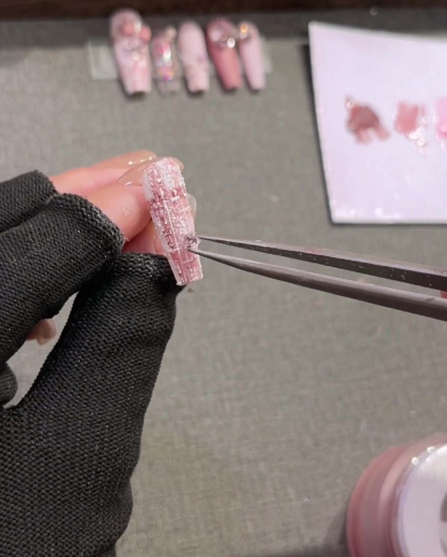 A pair of tweezers placing small decorative rhinestones onto a textured, plaid-painted nail tip.