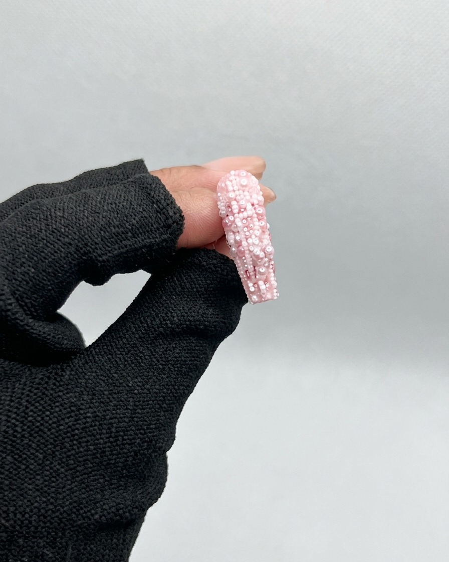 A brush applying a clear, glossy base gel to an unpainted, clear plastic nail tip.
