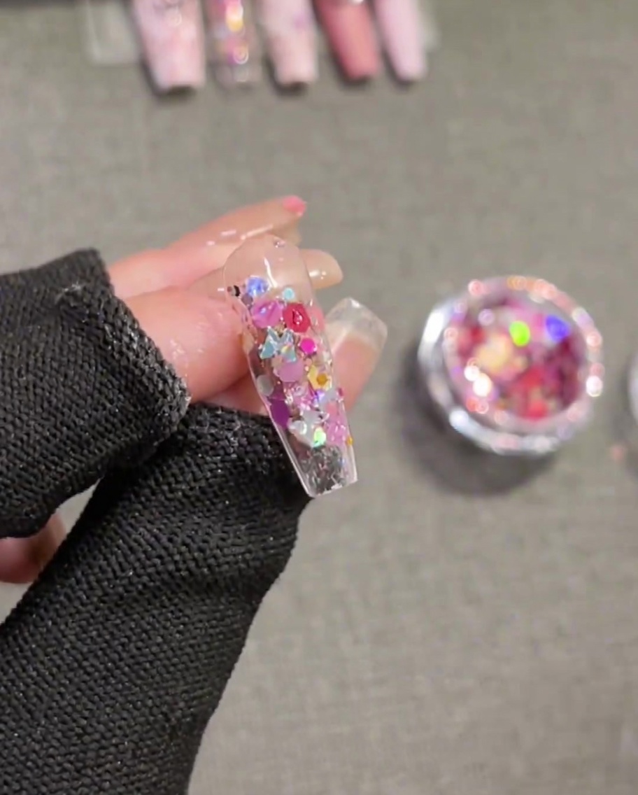 A brush applying a clear, thick consistency builder gel over a sequin-decorated nail, smoothing it out to create a level surface.