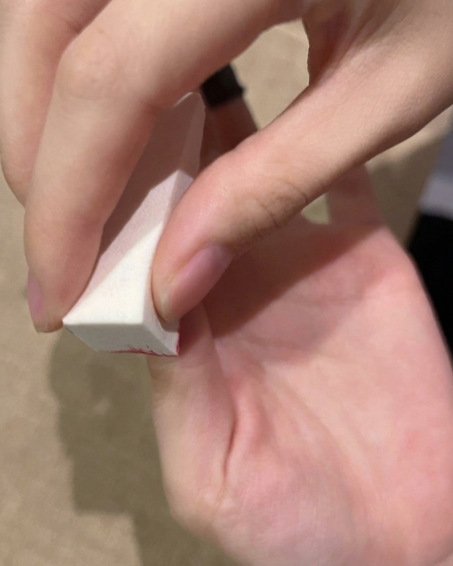 A hand patting gel on a nail with a sponge before curing under a UV lamp.