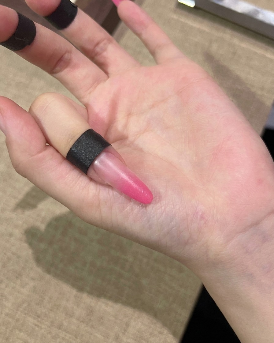A brush applying a coat of pink cat-eye gel over the entire surface of a nail.
