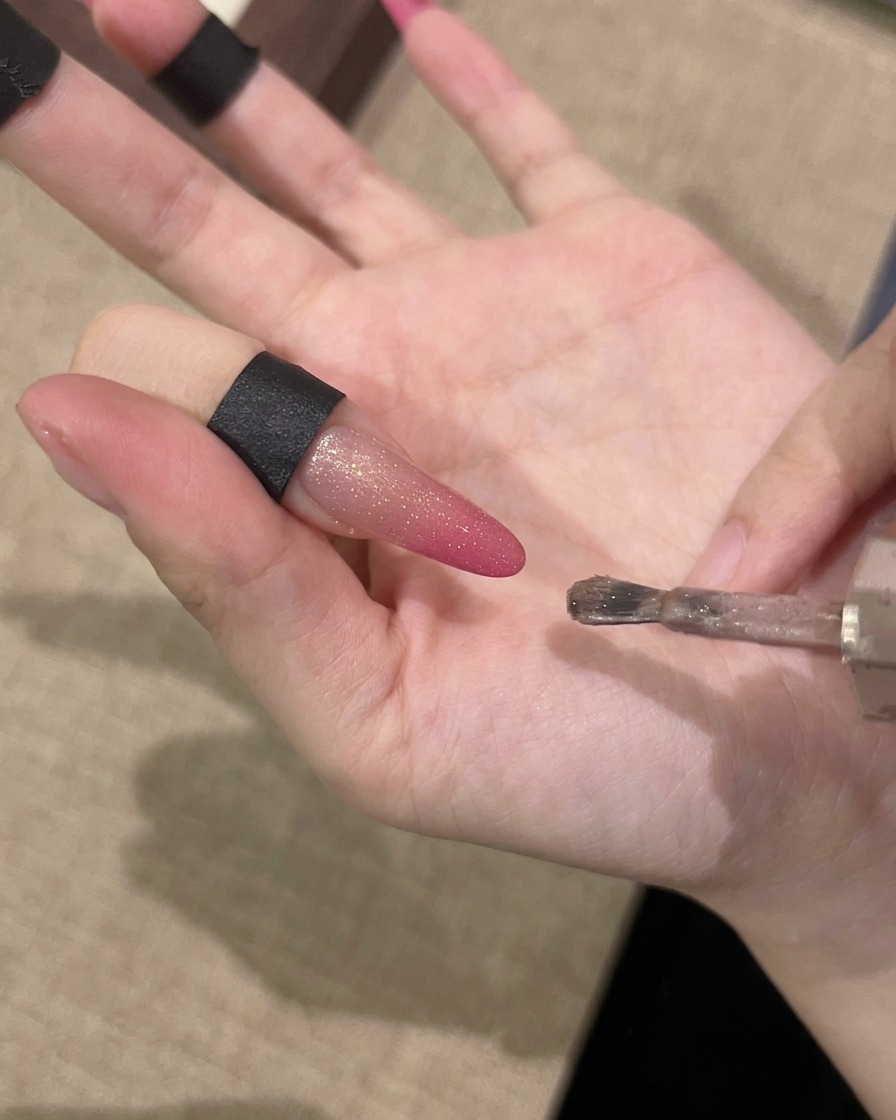 A hand holding a magnet parallel to a nail to attract magnetic shimmer particles.