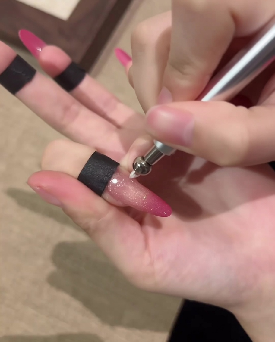 A close-up of a nail being manipulated with a magnetic pen tool to form a circular cat-eye orb effect.