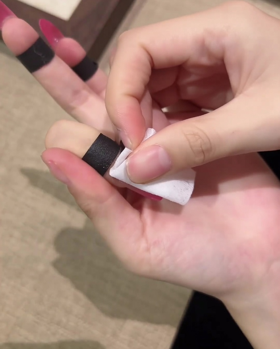 A hand using a lint-free cotton pad to wipe down a cured nail to remove the tacky layer.