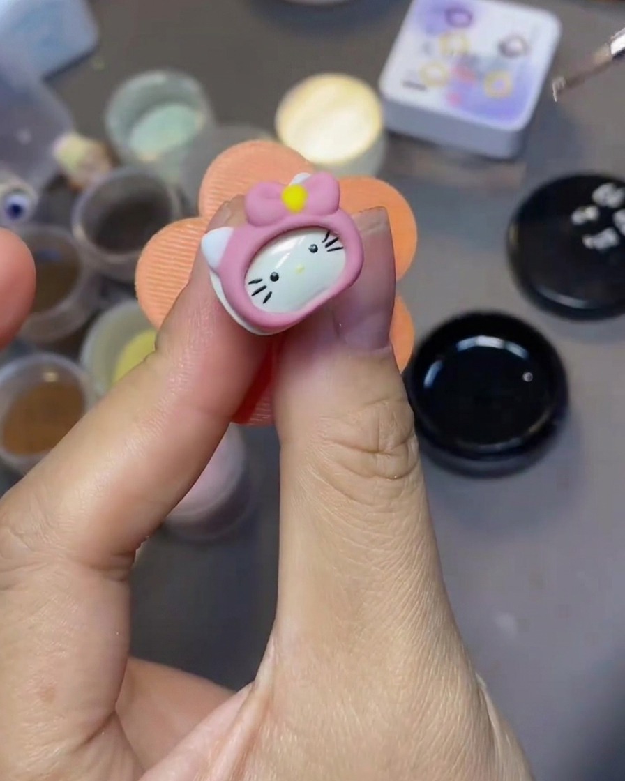 A fine nail art brush applying clear top coat over a 3D Hello Kitty nail charm.