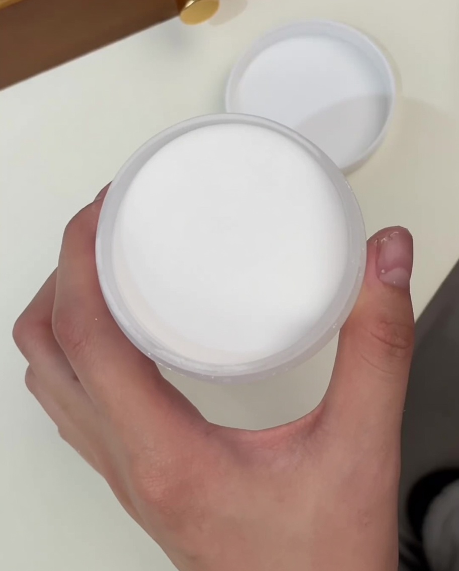 A top-down view of a hand holding an open jar of fine, clear crystal powder.